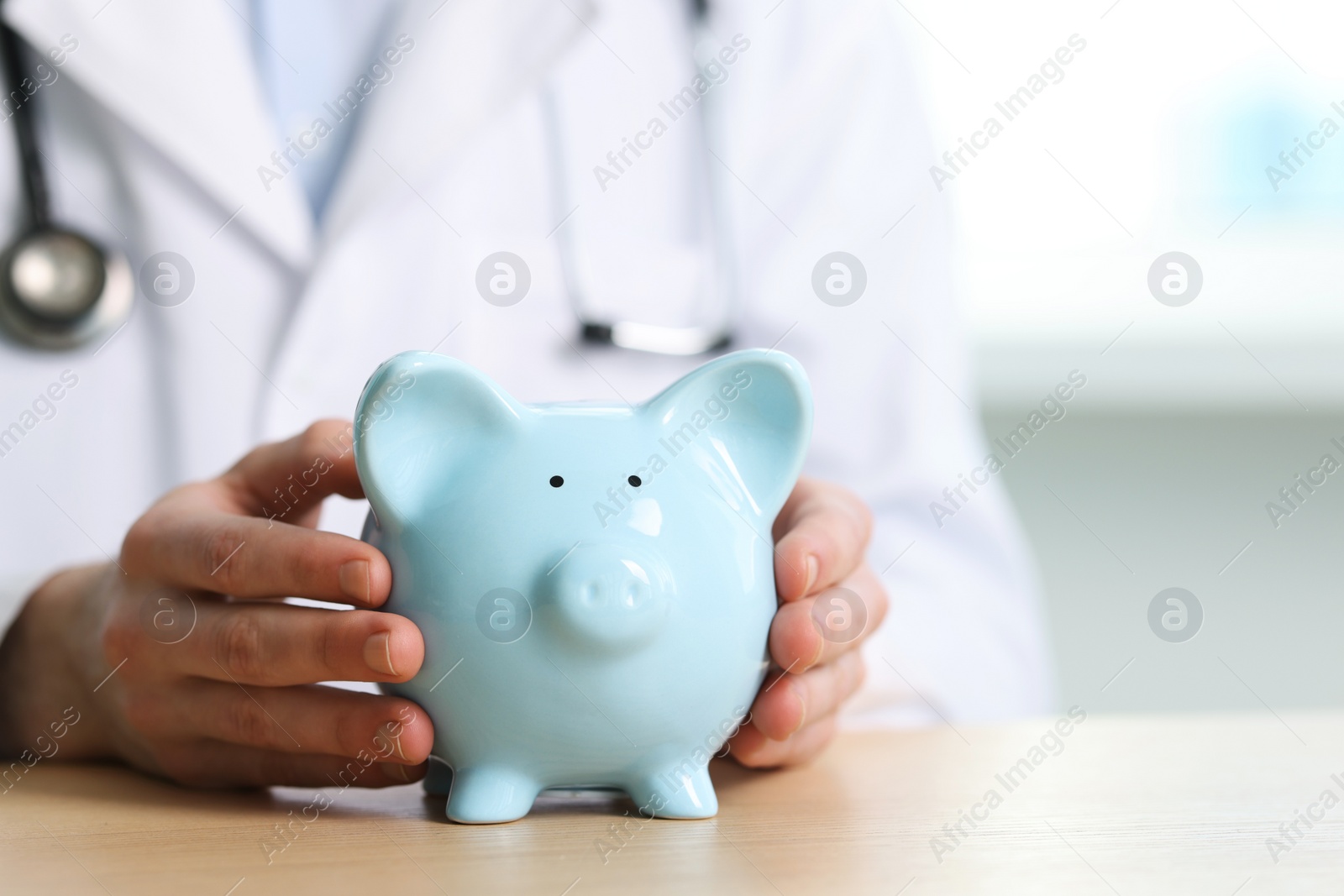 Photo of Doctor with piggy bank at wooden table, closeup