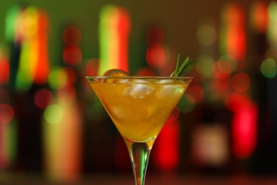 Martini glass with cocktail, ice cubes and rosemary in bar, closeup