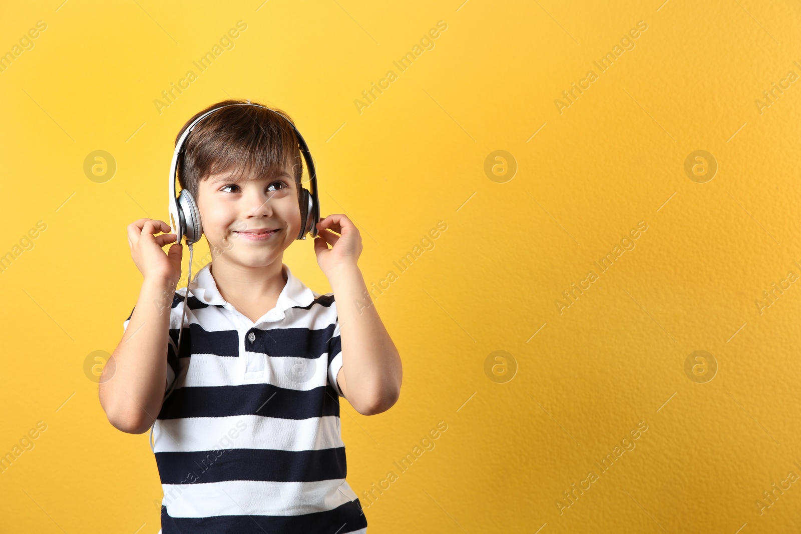 Photo of Cute little boy listening to music with headphones on color background. Space for text