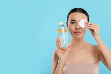 Beautiful woman removing makeup with cotton pad on light blue background, space for text