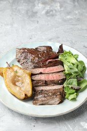 Photo of Pieces of delicious roasted beef meat, caramelized pear and greens on light textured table