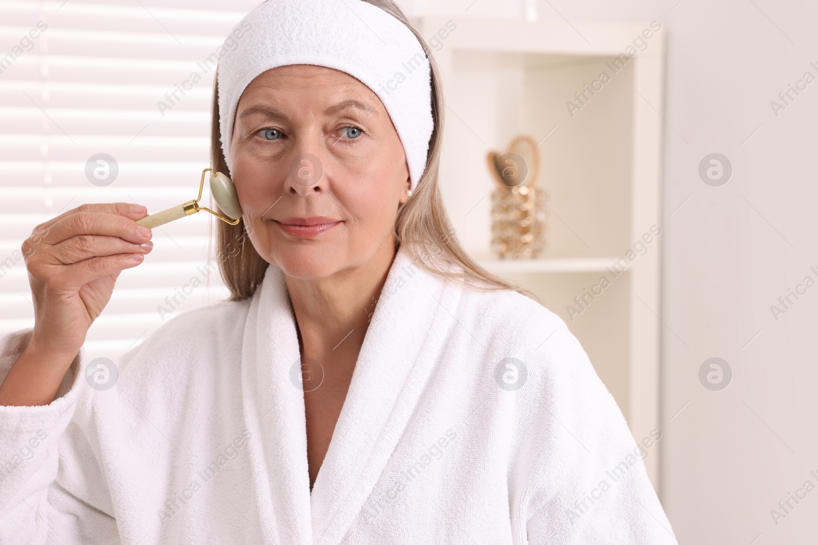 Photo of Woman massaging her face with jade roller in bathroom