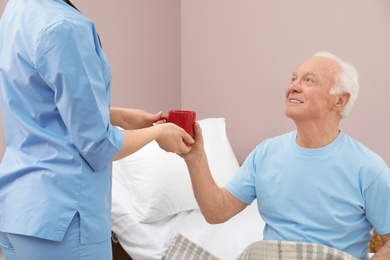 Nurse giving drink to senior man in hospital ward. Medical assisting