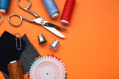 Flat lay composition with thimbles and different sewing tools on orange background, space for text