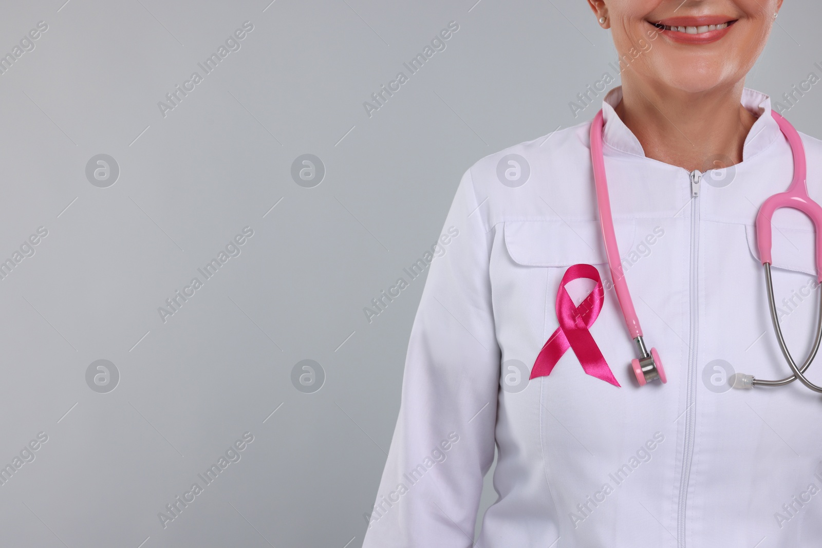 Photo of Doctor with pink ribbon and stethoscope on light grey background, closeup and space for text. Breast cancer awareness