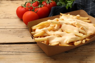 Delicious French fries with cheese sauce on wooden table, closeup