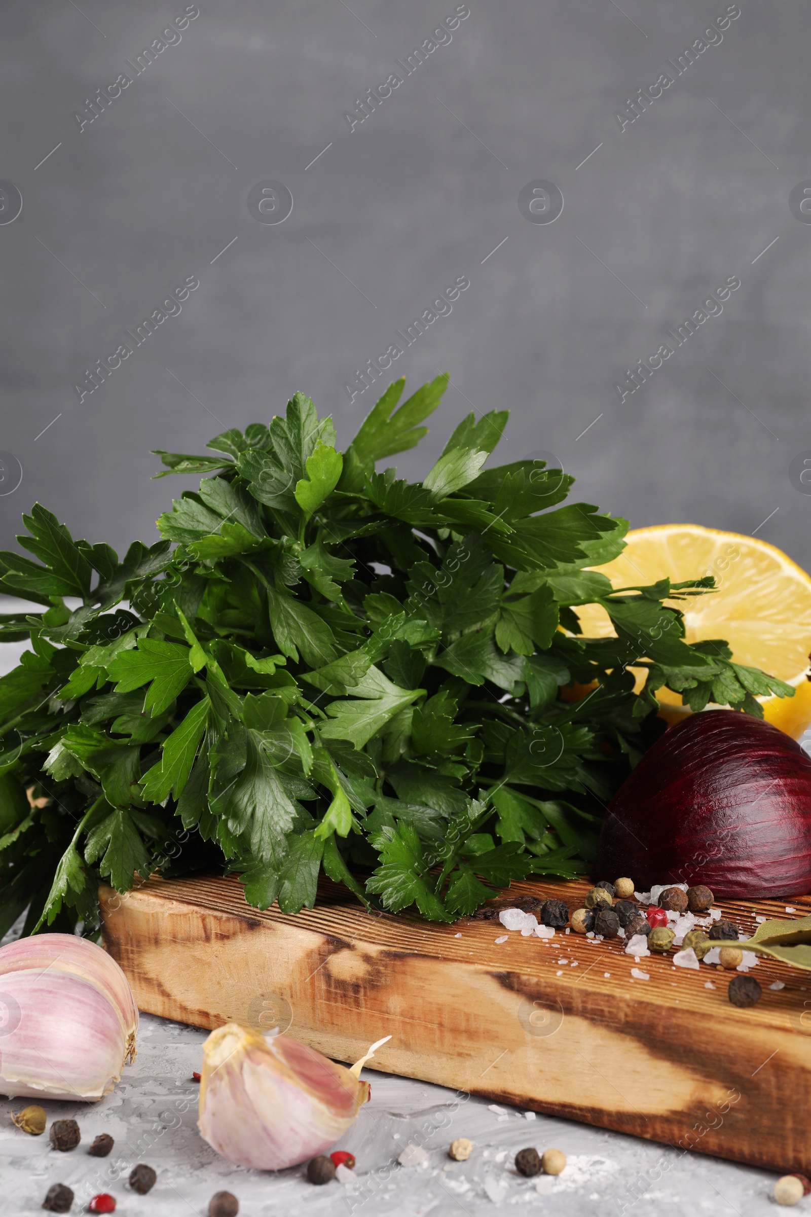 Photo of Bunch of fresh parsley, lemon, onion, garlic and spices on grey textured table