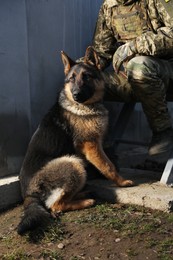 Photo of Ukrainian soldier with dog sitting outdoors, closeup
