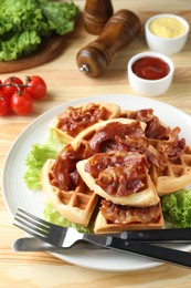 Photo of Tasty Belgian waffles served with bacon, lettuce and sauces on wooden table, closeup