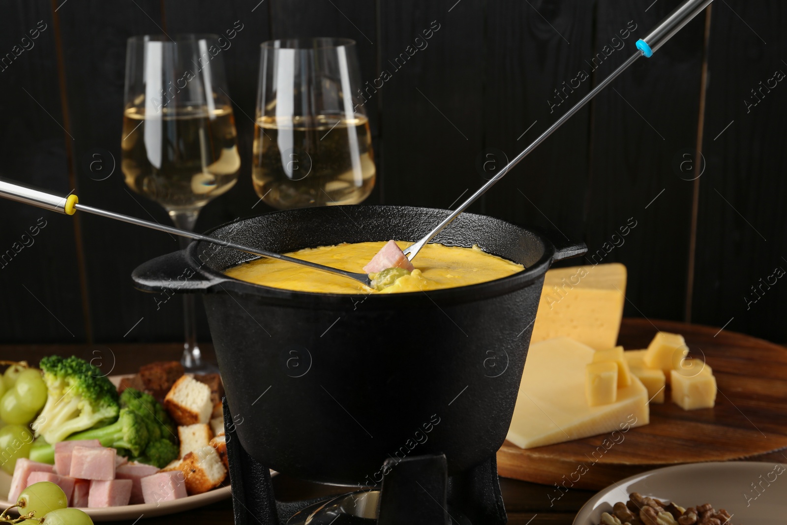 Photo of Fondue pot with melted cheese, forks and different products on wooden table, closeup