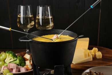 Photo of Fondue pot with melted cheese, forks and different products on wooden table, closeup