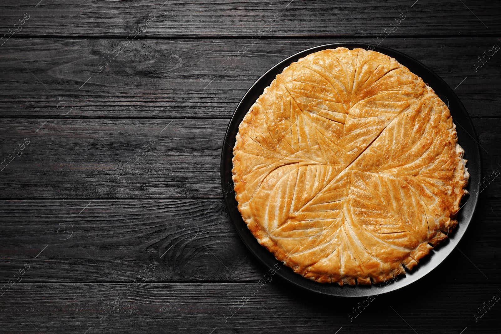 Photo of Traditional galette des rois on black wooden table, top view. Space for text