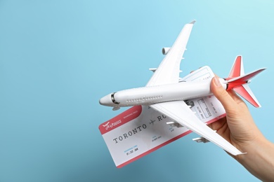 Photo of Woman holding toy airplane and tickets on light blue background, closeup