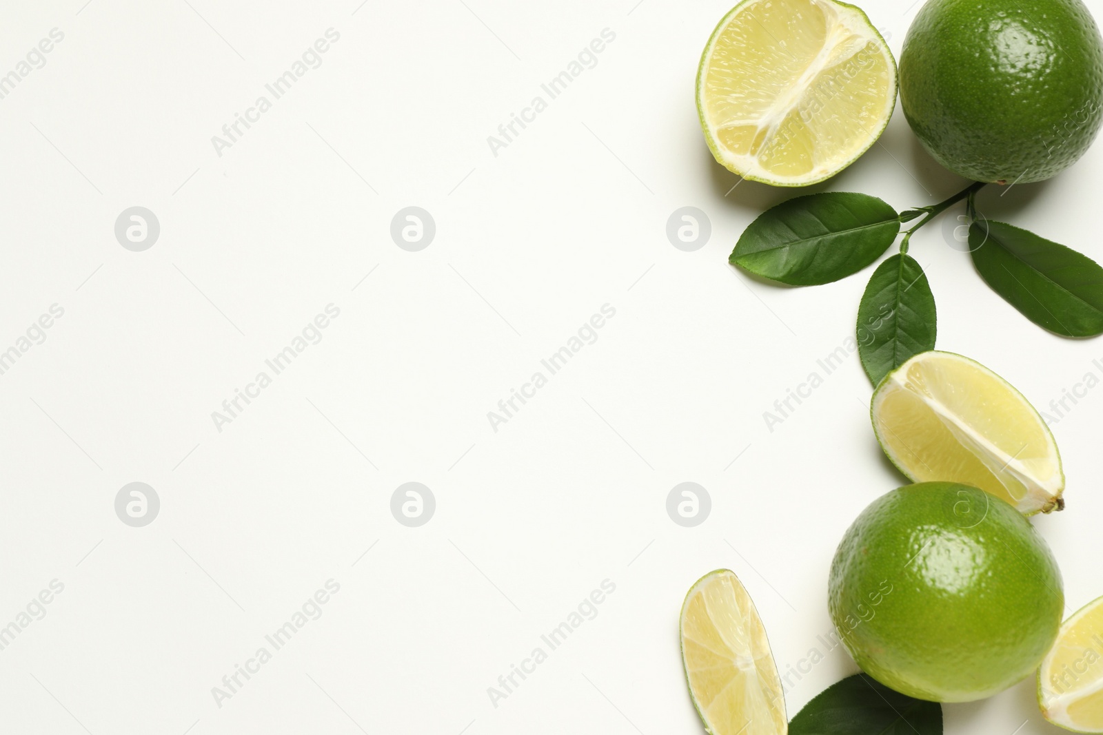 Photo of Whole and cut fresh ripe limes with green leaves on white background, flat lay