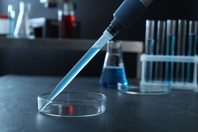 Photo of Laboratory analysis. Micropipette with liquid and petri dish on black table