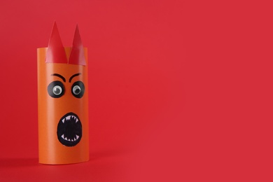 Photo of Funny orange monster on red background, space for text. Halloween decoration