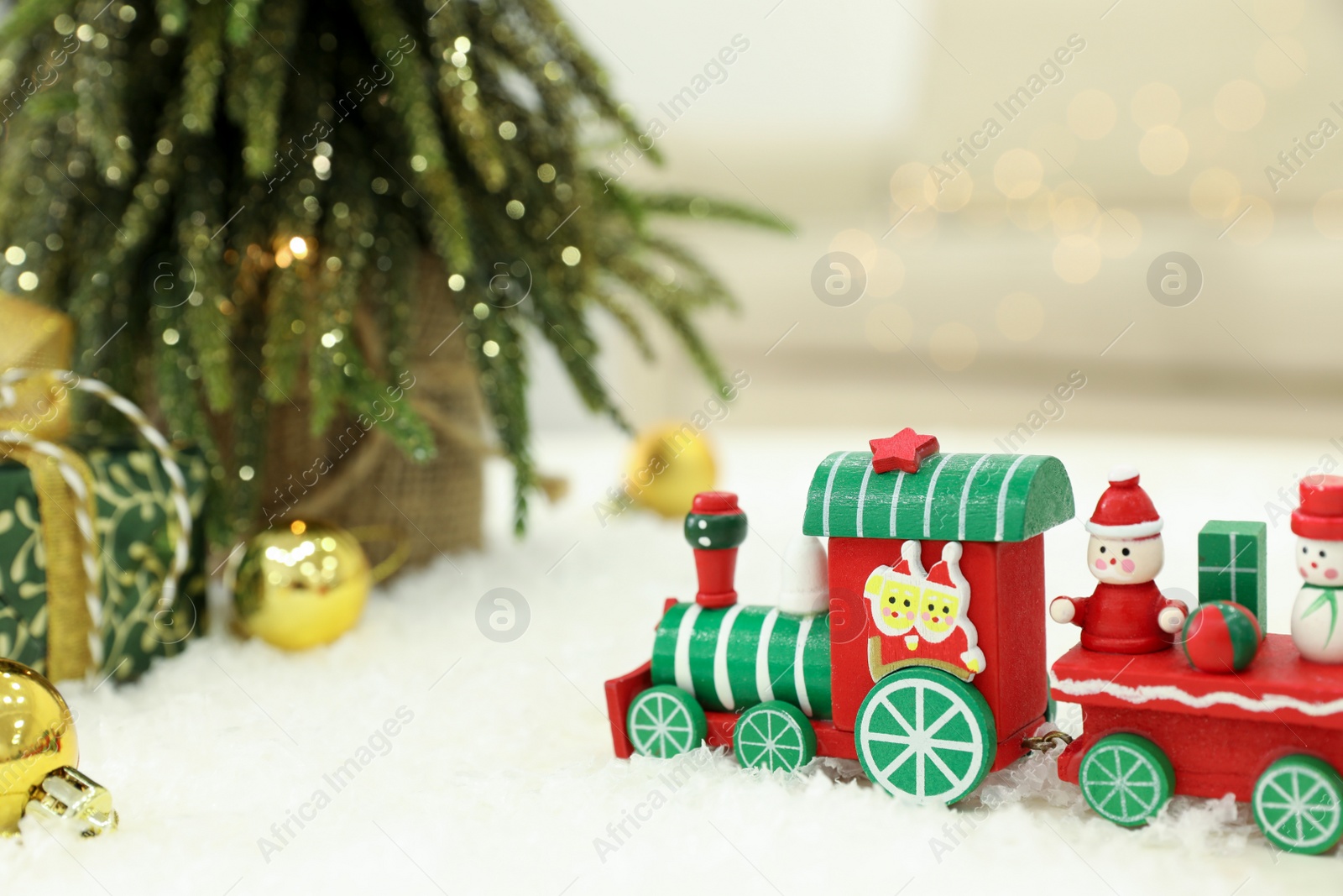 Photo of Bright toy train on artificial snow near small Christmas tree