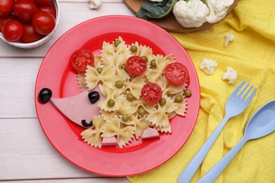 Photo of Creative serving for kids. Plate with cute hedgehog made of delicious pasta, sausages and tomatoes on white wooden table, flat lay