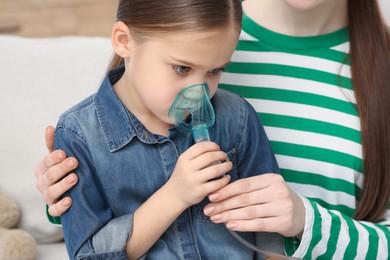 Photo of Mother helping her sick daughter with nebulizer inhalation at home