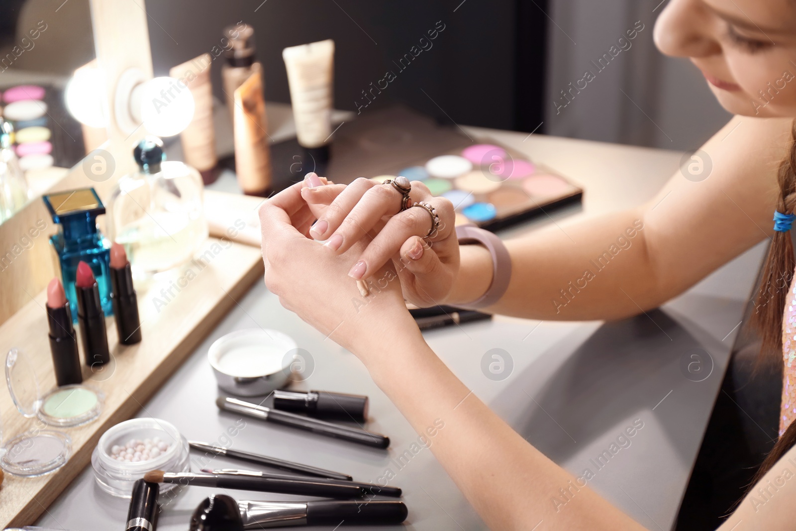 Photo of Young woman applying foundation on her hand in makeup room, closeup