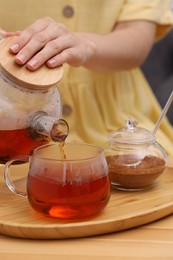 Photo of Woman pouring aromatic hot tea into glass cup at wooden table, closeup