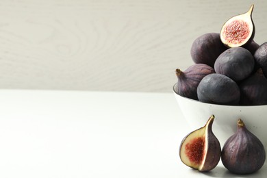 Whole and cut tasty fresh figs on white table. Space for text