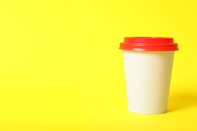 Photo of Takeaway paper coffee cup on yellow background, closeup. Space for text