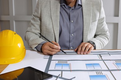 Architect working with construction drawings indoors, closeup