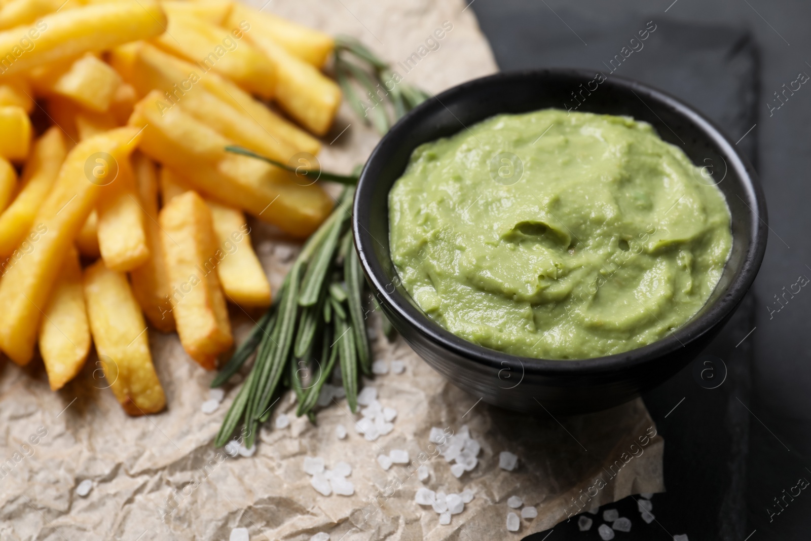 Photo of Serving board with french fries, guacamole dip and rosemary on black table, closeup