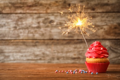Photo of Delicious birthday cupcake with sparkler on table