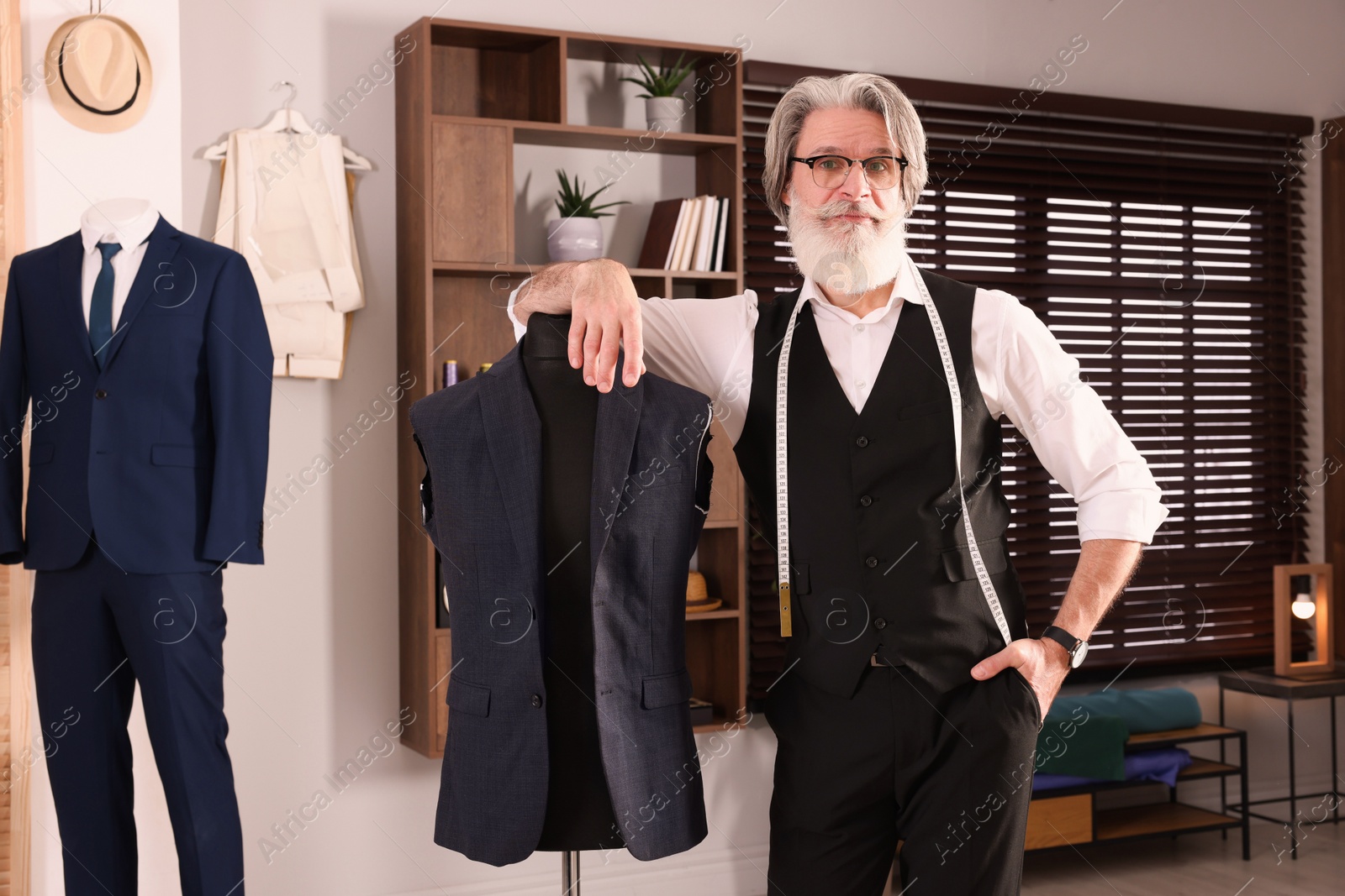 Photo of Professional tailor with measuring tape near mannequin in workshop