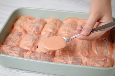 Photo of Woman pouring sauce onto uncooked stuffed cabbage rolls at white wooden table, closeup