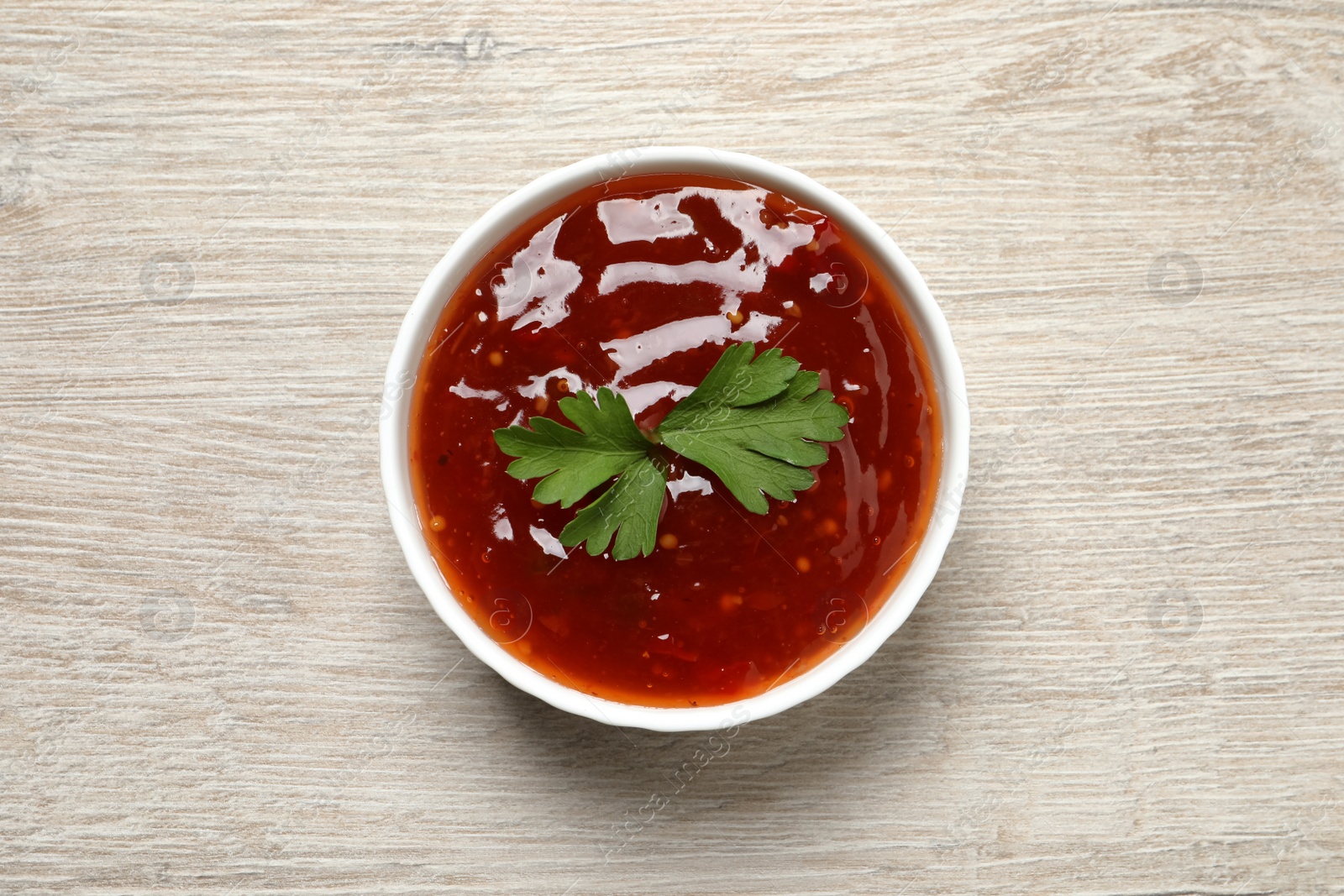 Photo of Spicy chili sauce with parsley in bowl on white wooden table, top view