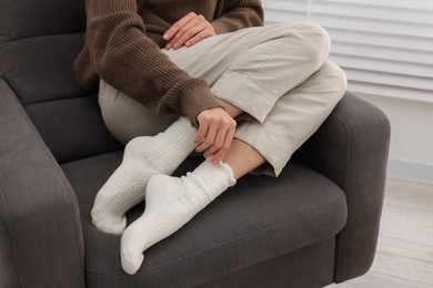 Photo of Woman in warm socks relaxing on armchair at home, closeup