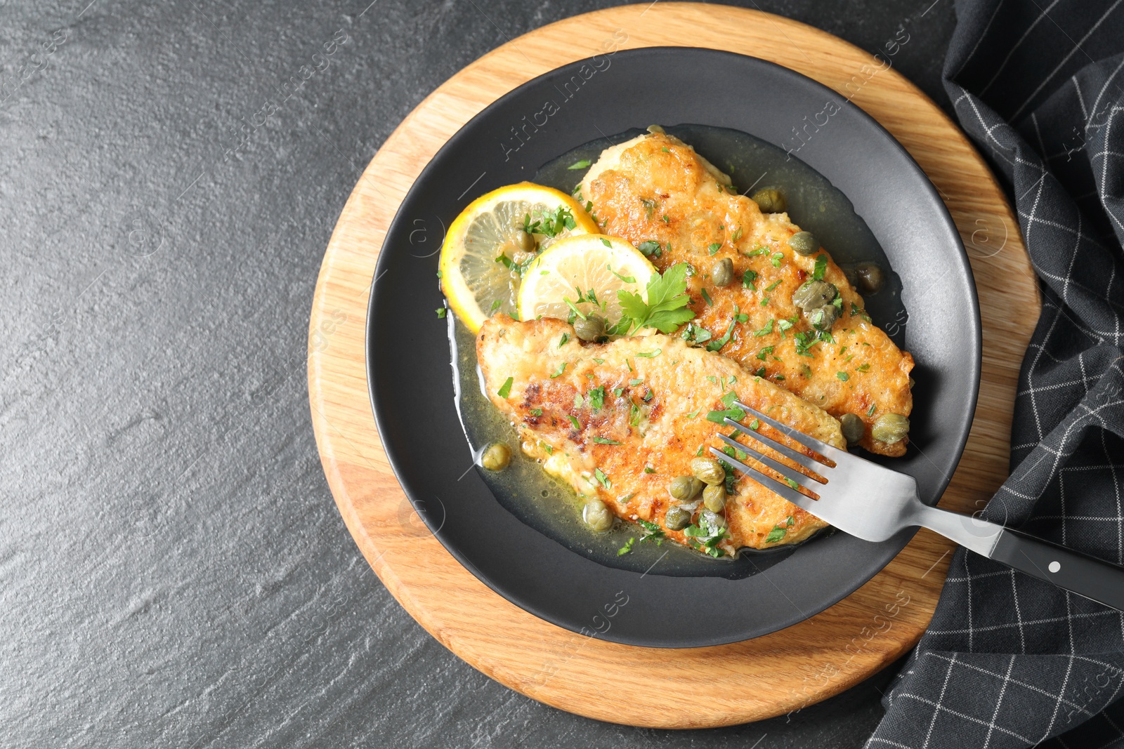 Photo of Delicious chicken piccata served on black table, top view