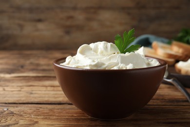 Photo of Bowl of tasty cream cheese and parsley on wooden table