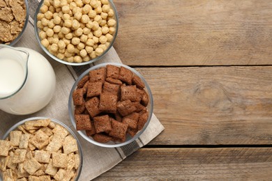 Photo of Different breakfast cereals and milk on wooden table, flat lay. Space for text