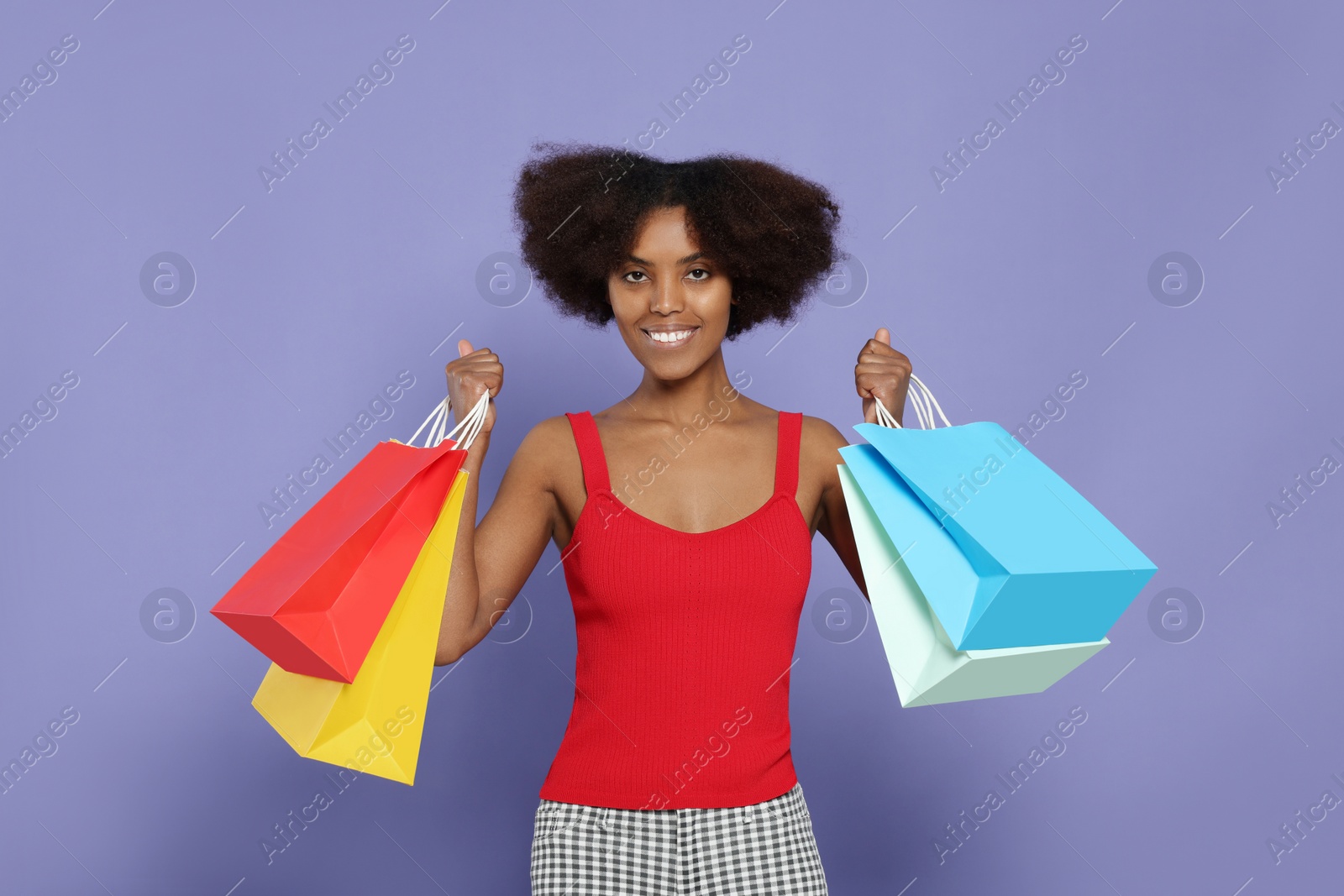 Photo of Happy African American woman with shopping bags on purple background