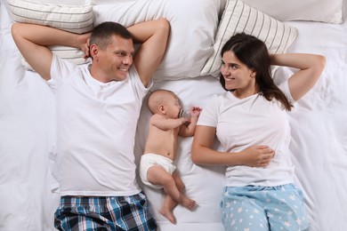 Photo of Cute baby sleeping near happy parents on bed, top view