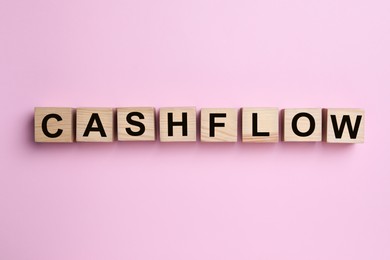 Image of Wooden cubes with phrase Cash FLow on pink background, flat lay