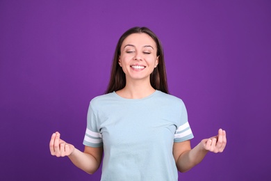 Photo of Young woman meditating on purple background. Stress relief exercise