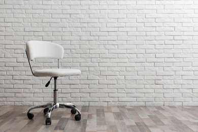 Photo of Comfortable office chair near white brick wall indoors. Space for text