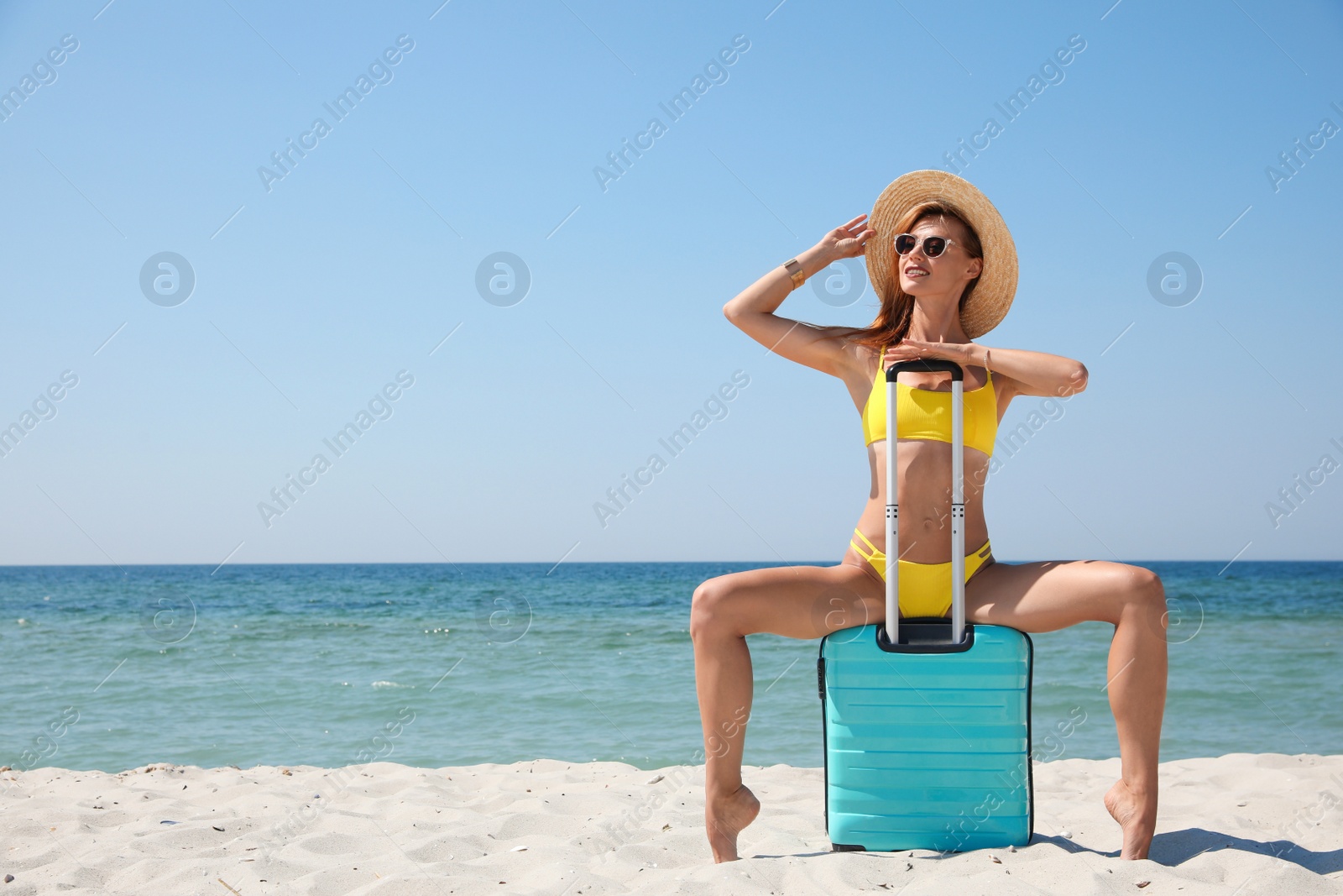 Photo of Attractive woman with suitcase posing on sandy beach near sea