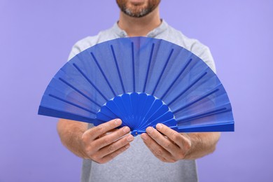 Photo of Man holding hand fan on purple background, closeup