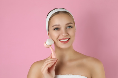 Photo of Young woman washing face with cleansing brush on pink background. Cosmetic product