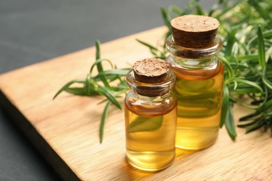 Photo of Bottles of essential oil and fresh rosemary sprigs on wooden board, closeup. Space for text