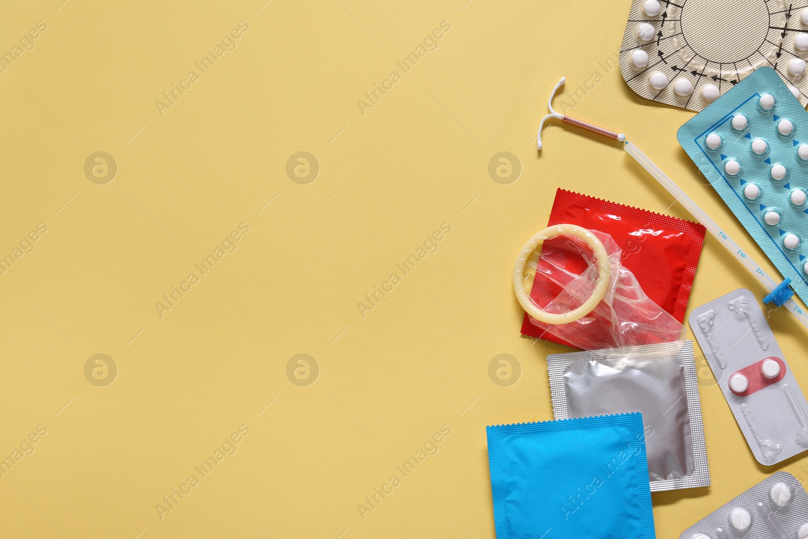 Photo of Contraceptive pills, condoms and intrauterine device on yellow background, flat lay with space for text. Different birth control methods