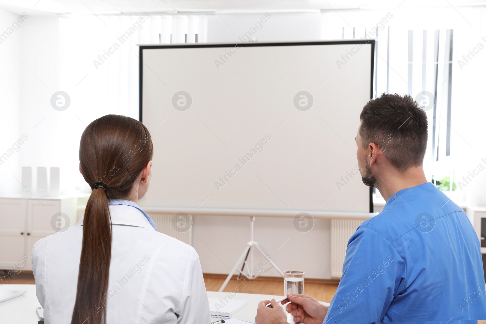 Photo of Team of doctors looking at projection screen indoors. 
Video conference