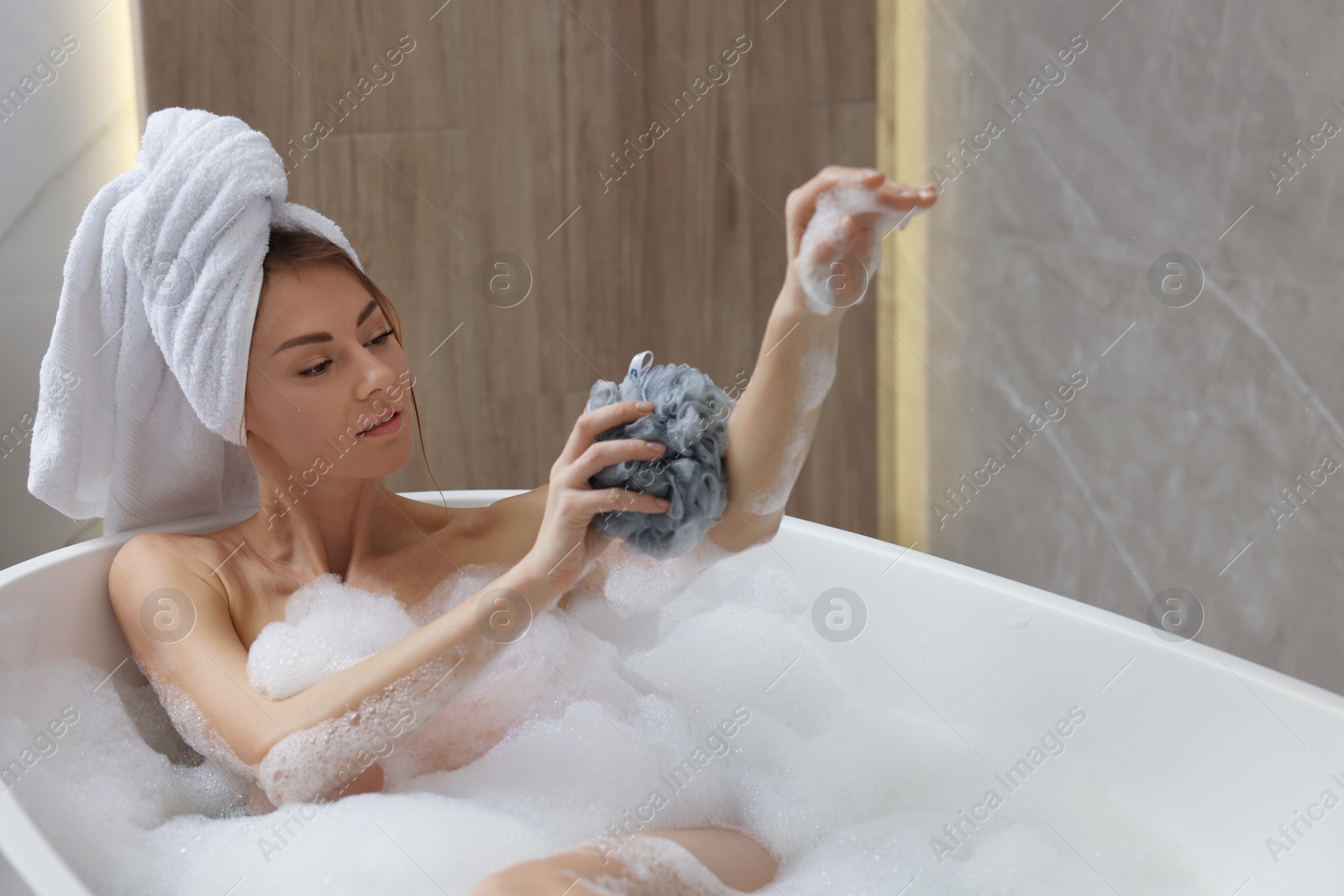 Photo of Beautiful woman with mesh pouf taking bath indoors