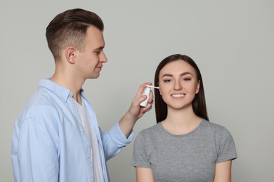 Man spraying medication into woman`s ear on light grey background